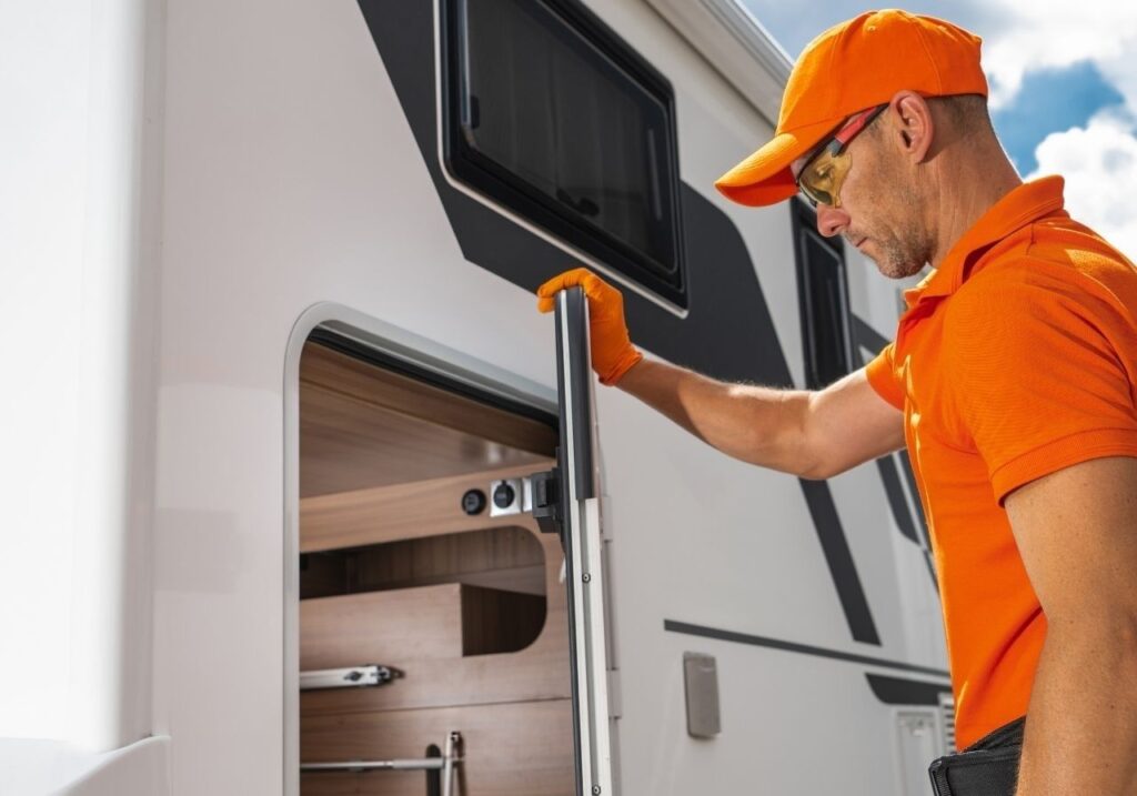 Close-up of RV systems being inspected: battery, fluid check, AC unit on rooftop